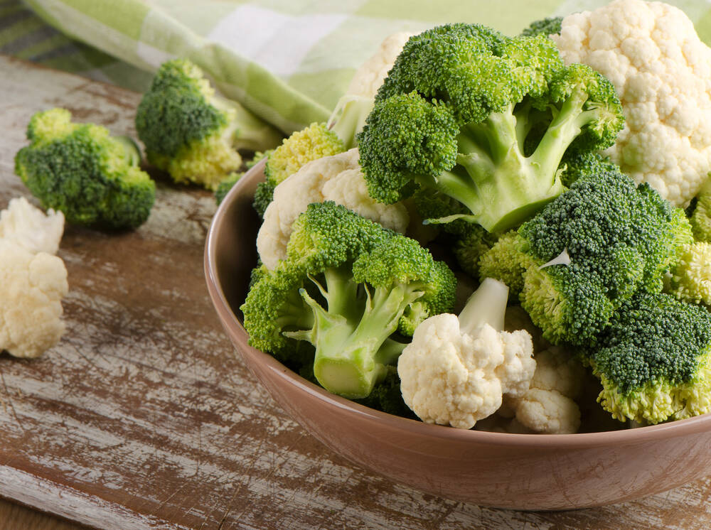 Bowl with fresh broccoli and cauliflower on a wooden table
